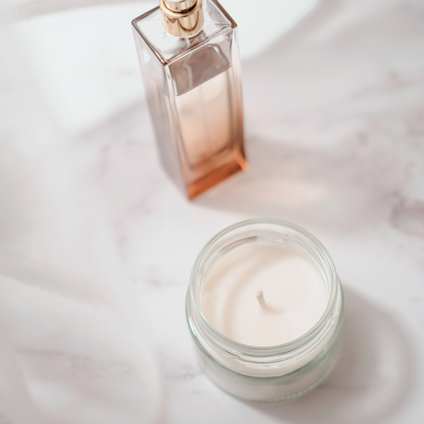Elegant amber perfume bottle and white candle on a marble surface – handcrafted fragrance and sensory objects for daily rituals